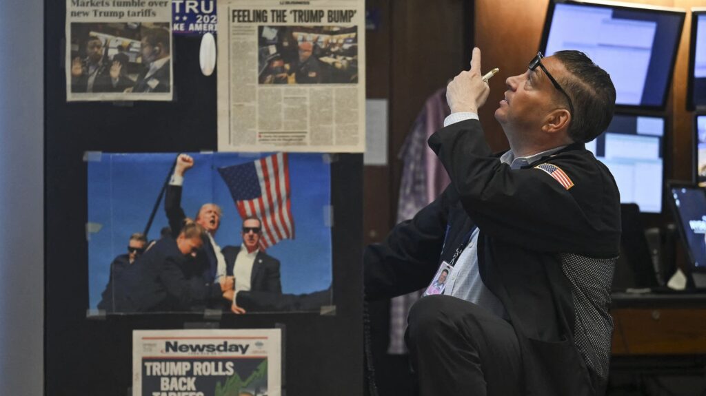 2fd164-20250423-a-new-york-stock-exchange-trader-points-upward-behind-newspaper-clippings-and-images-of-president-donald-trump-2000