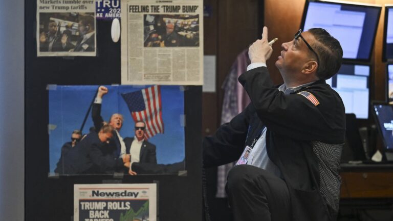 2fd164-20250423-a-new-york-stock-exchange-trader-points-upward-behind-newspaper-clippings-and-images-of-president-donald-trump-2000